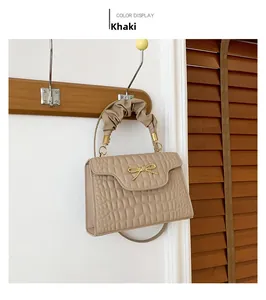 Close-up of khaki crocodile pattern handbag featuring a gold woven bow and pleated handle