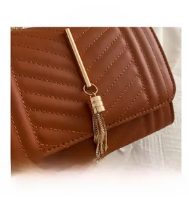 Close-up of brown quilted crossbody bag with V-pattern stitching and gold chain tassel