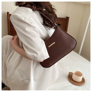 Détail d'un sac sous le bras en cuir marron foncé avec boucle dorée et sangle nouée