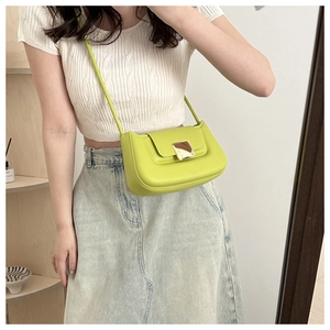 Lime green crossbody bag with gold buckle detail worn by a model in casual white outfit