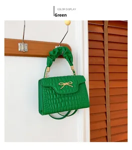 Detail of green crocodile texture handbag with gold metal bow and pleated handle