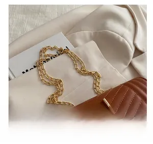 Detail of golden double chain strap on caramel V-quilted small square shoulder bag