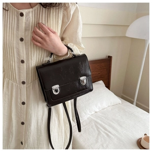 Brown vintage messenger bag with double silver metal buckles shown in bedroom setting