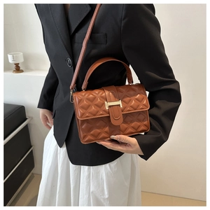 Detailed view of brown quilted crossbody bag with gold hardware held by a fashion model