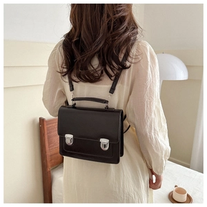 Détail d'un cartable rétro en cuir noir avec boucles argentées et porté à l'épaule