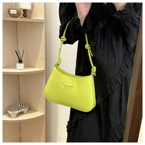 Detail of neon green crescent shoulder bag with knotted strap and gold hardware accents