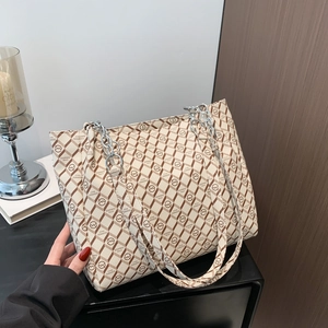 Large beige and brown checkered tote bag with metal chain straps on a dark surface