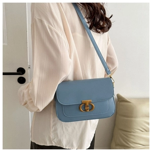 Détail du sac carré en cuir PU bleu avec fermoir doré porté à l'épaule du modèle