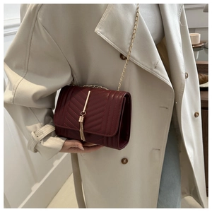 Detail of burgundy quilted shoulder bag with gold chain strap and elegant tassel