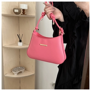Close-up of a pink leather handbag with a unique knotted handle and gold metal accents