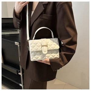 Detail of white quilted crossbody bag with gold buckle worn with a dark blazer
