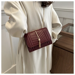 Detail of burgundy chevron quilted bag featuring gold chain and metallic tassel