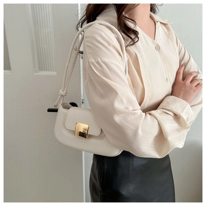 Detail of creamy white underarm bag with gold square clasp and knotted strap detail