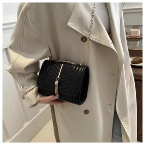 Detail of black quilted leather crossbody bag with elegant gold chain and tassel pendant