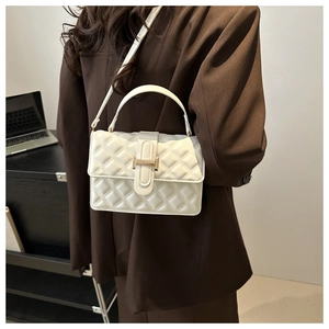 Close-up of white quilted crossbody bag with H-shaped gold buckle worn on a brown blazer
