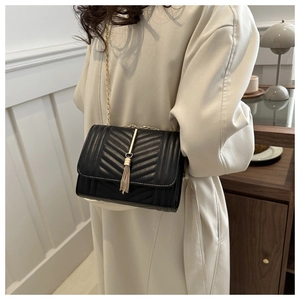 Detail of black quilted crossbody bag with gold chain strap and metal tassel charm