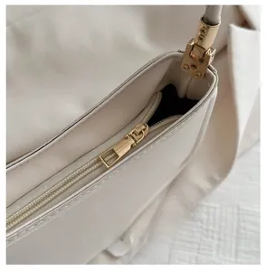 Detail of smooth gold zipper and hardware on a minimalist cream white leather handbag