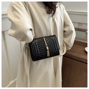 Detail of black chevron quilted crossbody bag with gold tassel and elegant chain strap