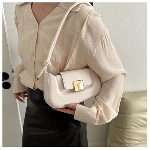 Close-up of minimalist white underarm bag with gold buckle on elegant model outfit
