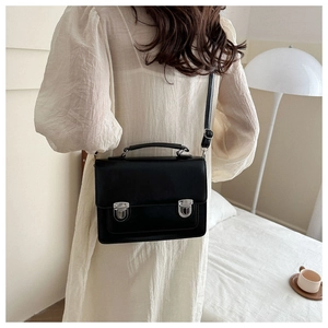 Detail of a black leather satchel bag with silver metal buckles on a white dress model