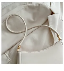 Close-up of cream leather shoulder bag with gold metal buckle and round handle detail