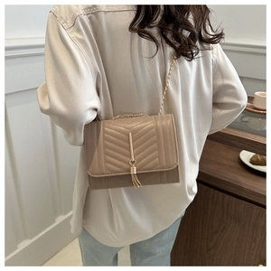 Detail of beige quilted crossbody bag with golden chain strap and tassel pendant