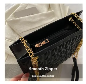 Close-up of smooth zipper closure and gold chain on black quilted shoulder bag