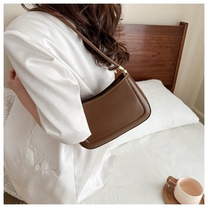 Detail of dark brown minimalist leather underarm bag with gold metal buckle hardware