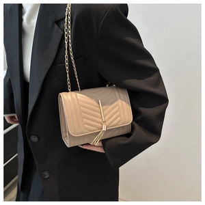 Detail of light beige quilted crossbody bag with gold tassel and elegant chain strap