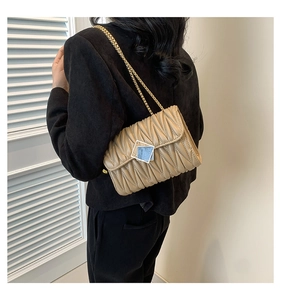 Détail du sac à chaîne matelassé beige avec fermoir doré porté par une femme
