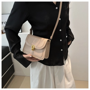Detail shot of beige faux leather square bag featuring a gold twist lock and slim strap