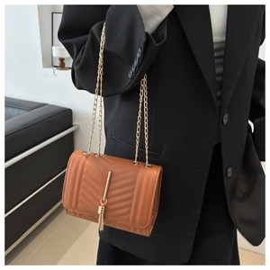 Close-up of caramel quilted chain crossbody bag with golden tassel detail and V-shaped stitching