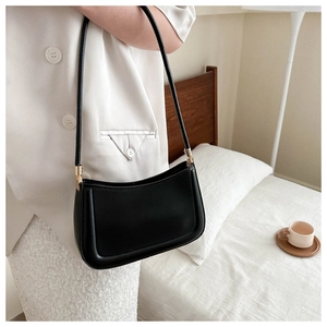 Detail of a black minimalist underarm bag with gold hardware and matte leather texture