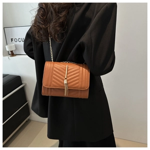 Detail of caramel brown crossbody bag with V-quilted texture and gold tassel on model