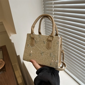 Straw handbag with floral embroidery and brown leather strap shown in a handheld view