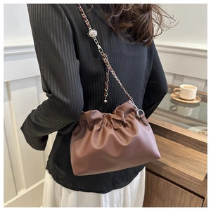 Detail of a brown pleated bucket bag featuring a gold-tone chain strap and decorative orb