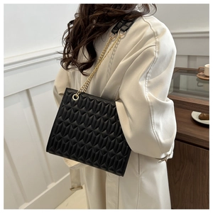 Quilted black leather shoulder bag with gold chain strap shown on model's shoulder