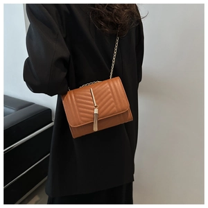 Detailed view of brown quilted crossbody bag with gold chain strap and tassel on model