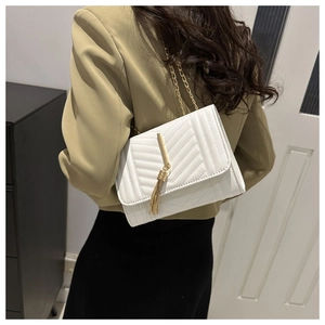 White quilted chain crossbody bag with gold tassel detail shown on model in khaki blazer