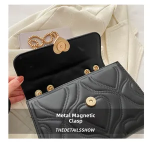 Detail of black quilted shoulder bag featuring heart-shaped gold metal magnetic clasp