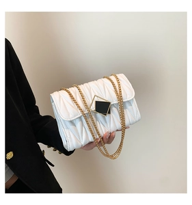 Détail du sac matelassé blanc avec boucle dorée tenu par un mannequin en costume noir