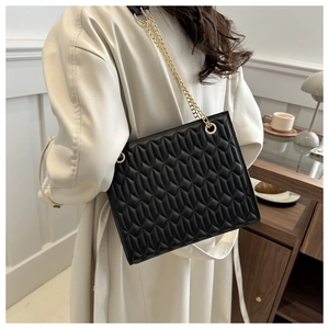 Close-up of quilted black chain bag with gold ring buckle against a cozy cafe background