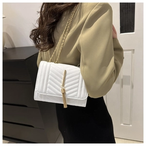 Detailed back view of a woman wearing a white V-quilted crossbody bag with gold tassel