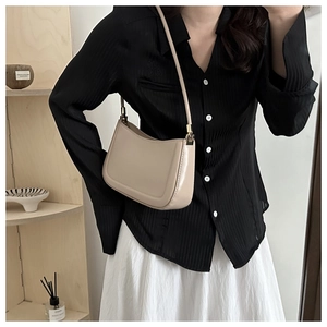 Minimalist beige leather shoulder bag with gold hardware shown in a lifestyle setting