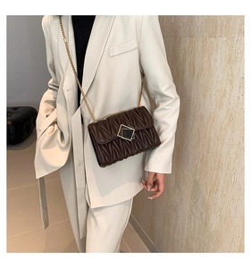 Détail d'un sac marron matelassé avec chaîne dorée sur une veste de costume crème