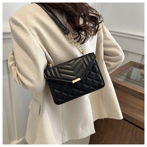 Detail shot of black quilted crossbody bag with gold chain strap on a white blazer
