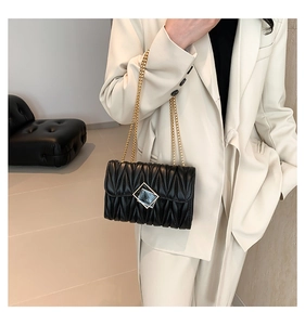 Détail du sac à bandoulière matelassé noir avec chaîne dorée porté par un mannequin chic
