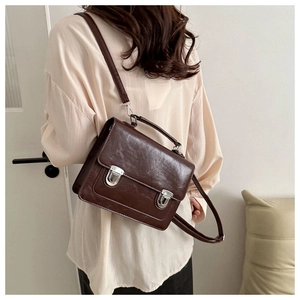 Détail d'un sac messager vintage marron foncé avec boucles argentées et texture cuir