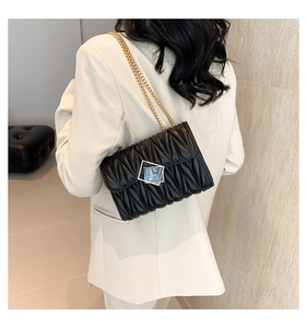 Détail du sac matelassé noir à chaîne et boucle dorée porté sur un blazer blanc