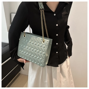 Detail of mint green quilted crossbody bag with golden chain strap on model